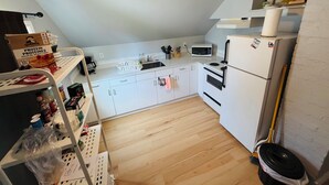 Een kleine kitchenette met witte kastjes, een magnetron, een koelkast en een plafondlamp.