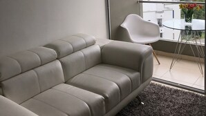 A modern living room with a beige sofa, a white chair, and a glass table with a vase of flowers. - APTO  LOFT   PEREIRA (Pereira)