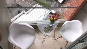 A balcony with two white chairs, a glass table with a vase of flowers, and a view of a brick building and a parked car. - APTO  LOFT   PEREIRA (Pereira)