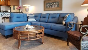 Ein Wohnzimmer mit einem blauen Sofa, einem runden Holztisch und einem Korbstuhl.