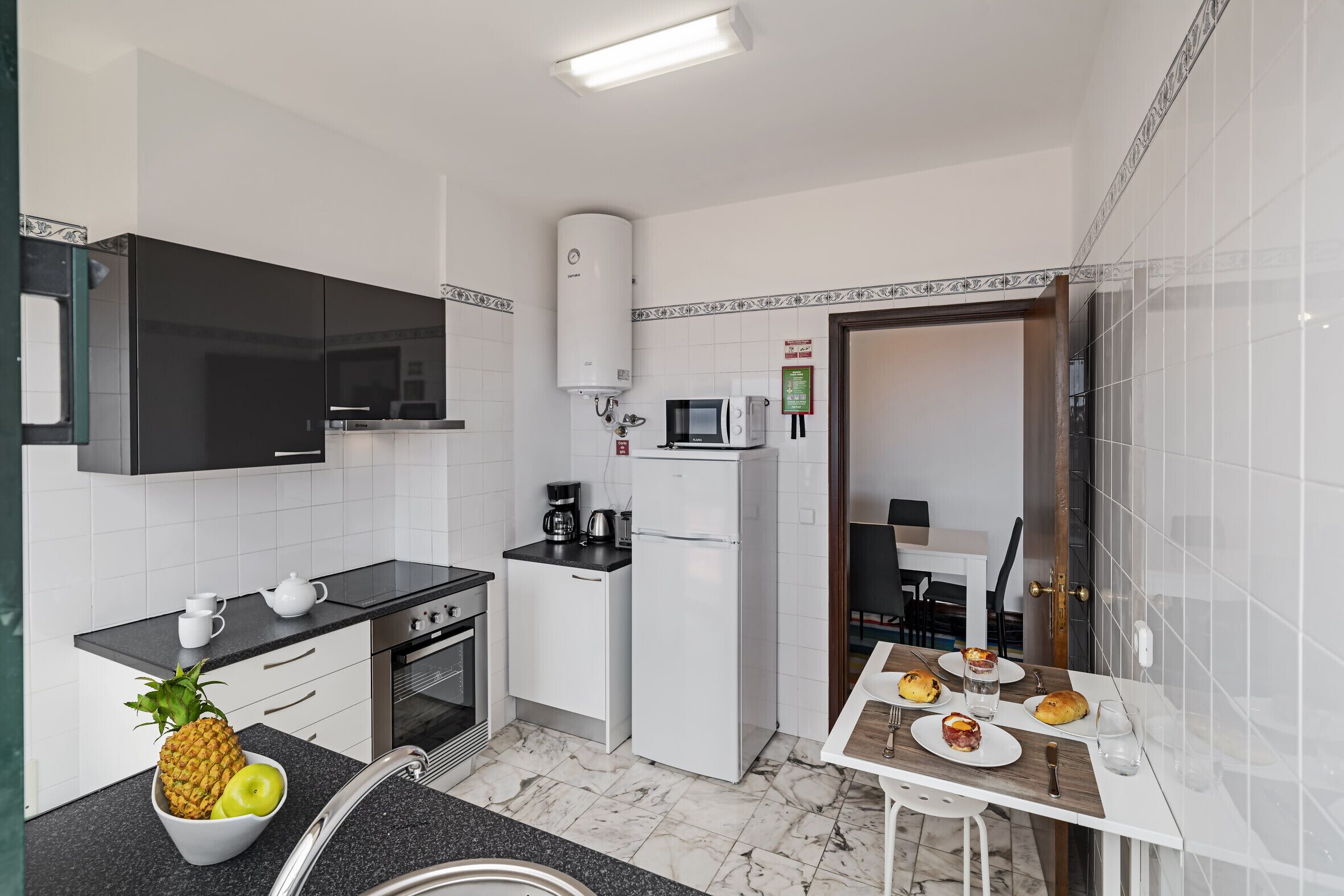Cocina compacta con microondas, refrigerador, estufa y un pequeño comedor con mesa para dos.
