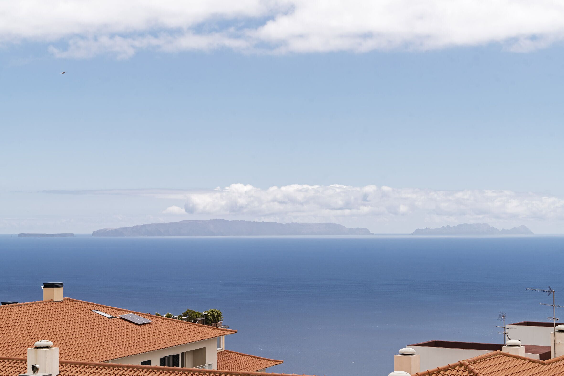 A coastal view with a clear sky, a distant mountain range, and a calm sea.