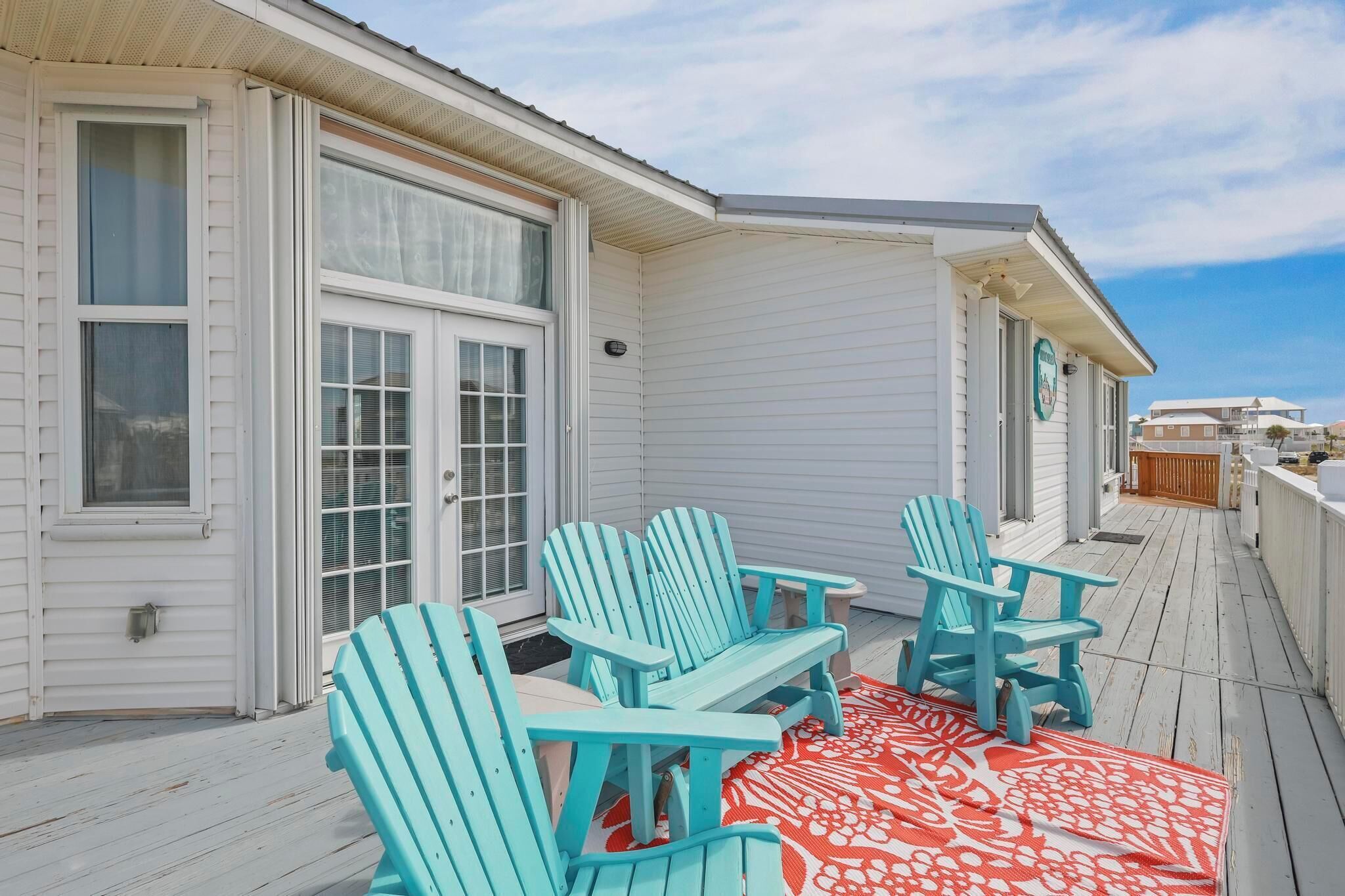 A covered outdoor area with a table and four turquoise Adirondack chairs.