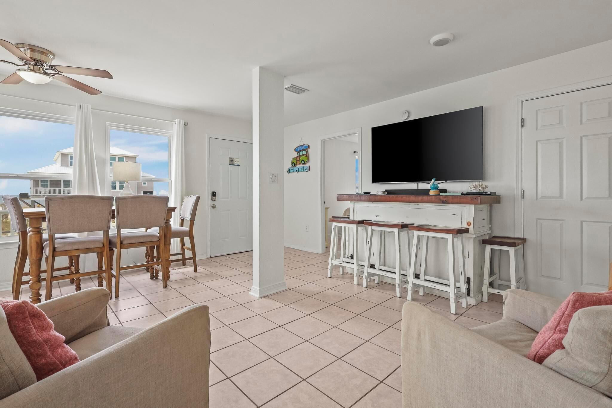 Ampla sala de estar com mesa de jantar, cadeiras, televisão e varanda com vista para uma casa.