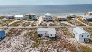 Une zone résidentielle côtière avec des maisons sur pilotis, une plage de sable et l’océan en arrière-plan.