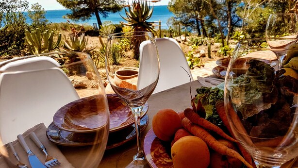Une table dressée pour un repas, avec vue sur la mer et les arbres.