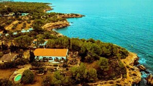 Vue aérienne d’une propriété située sur la côte, avec une grande maison, une piscine et une végétation luxuriante.