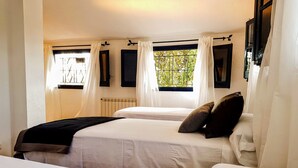 Une chambre avec deux lits, du linge de lit blanc, un radiateur et des fenêtres avec des rideaux.