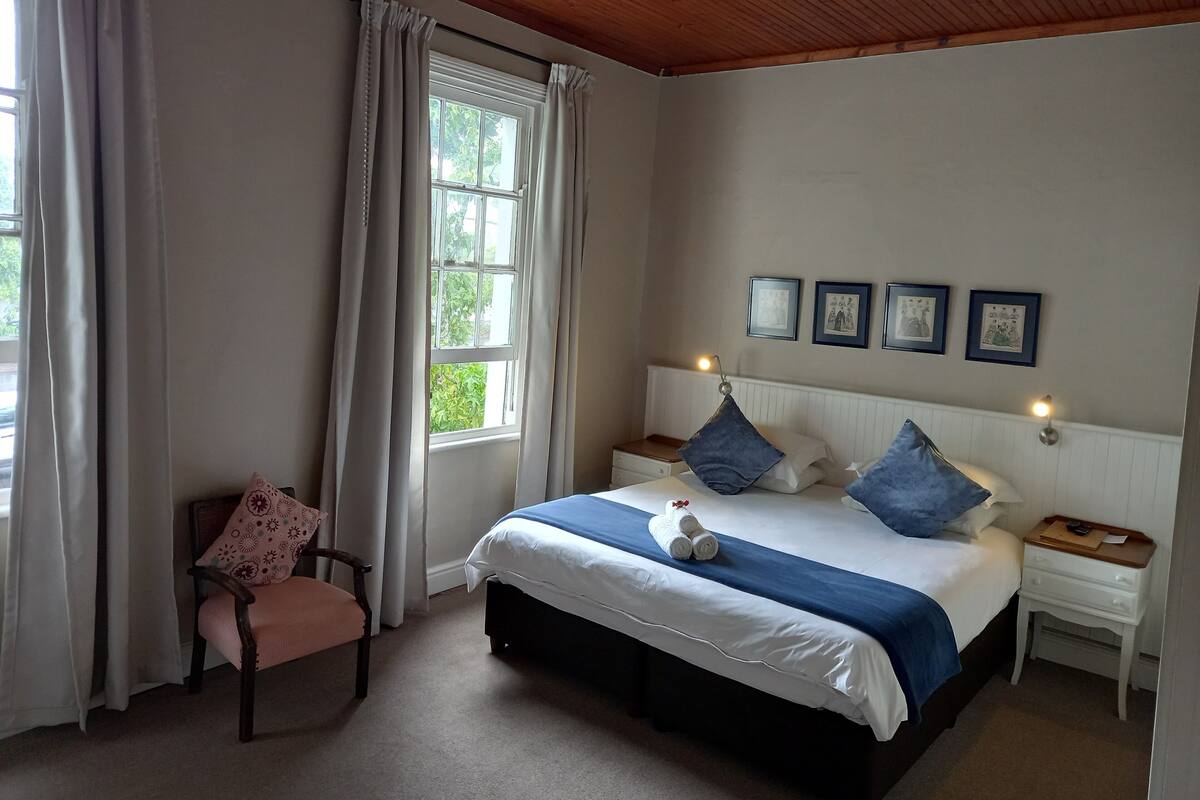 A bedroom with a bed, a chair, a nightstand, and a window with curtains.