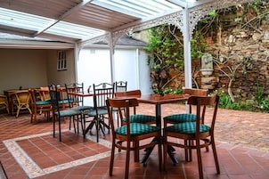 Un patio al aire libre con zona de estar cubierta, paredes de piedra y barandilla blanca decorativa.