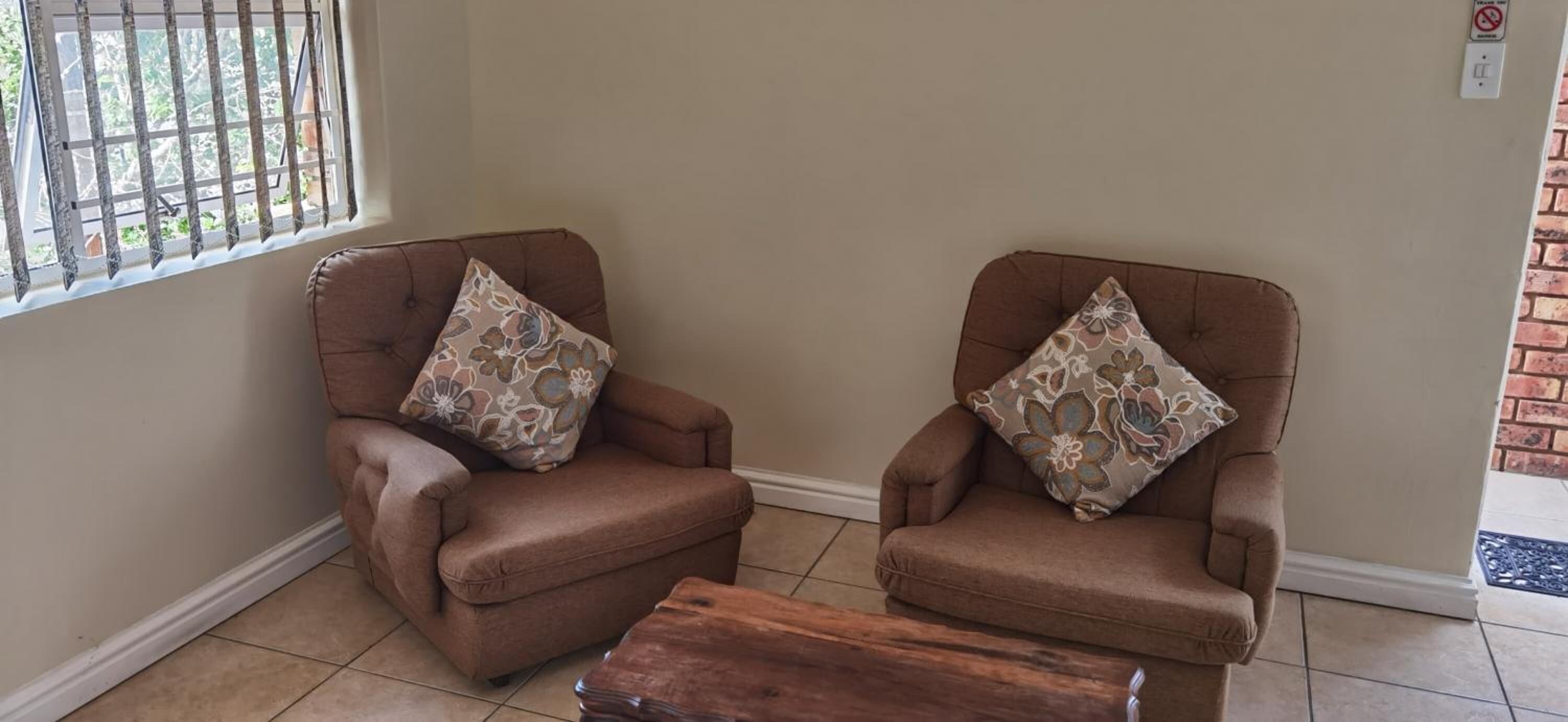 Two brown armchairs with floral cushions, a wooden coffee table, and a window with metal bars.