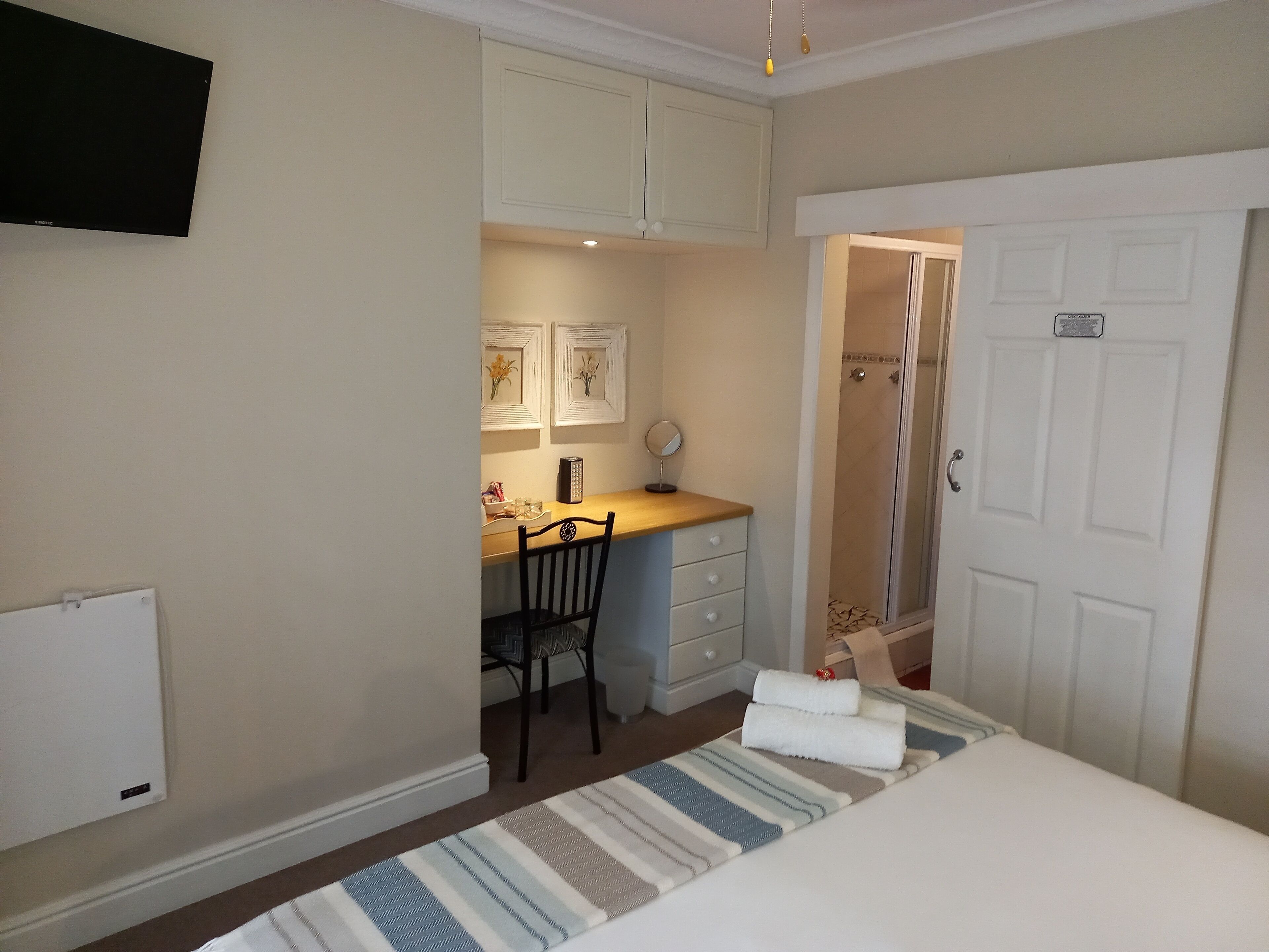 A bedroom with a bed, a desk, a chair, and a shower.