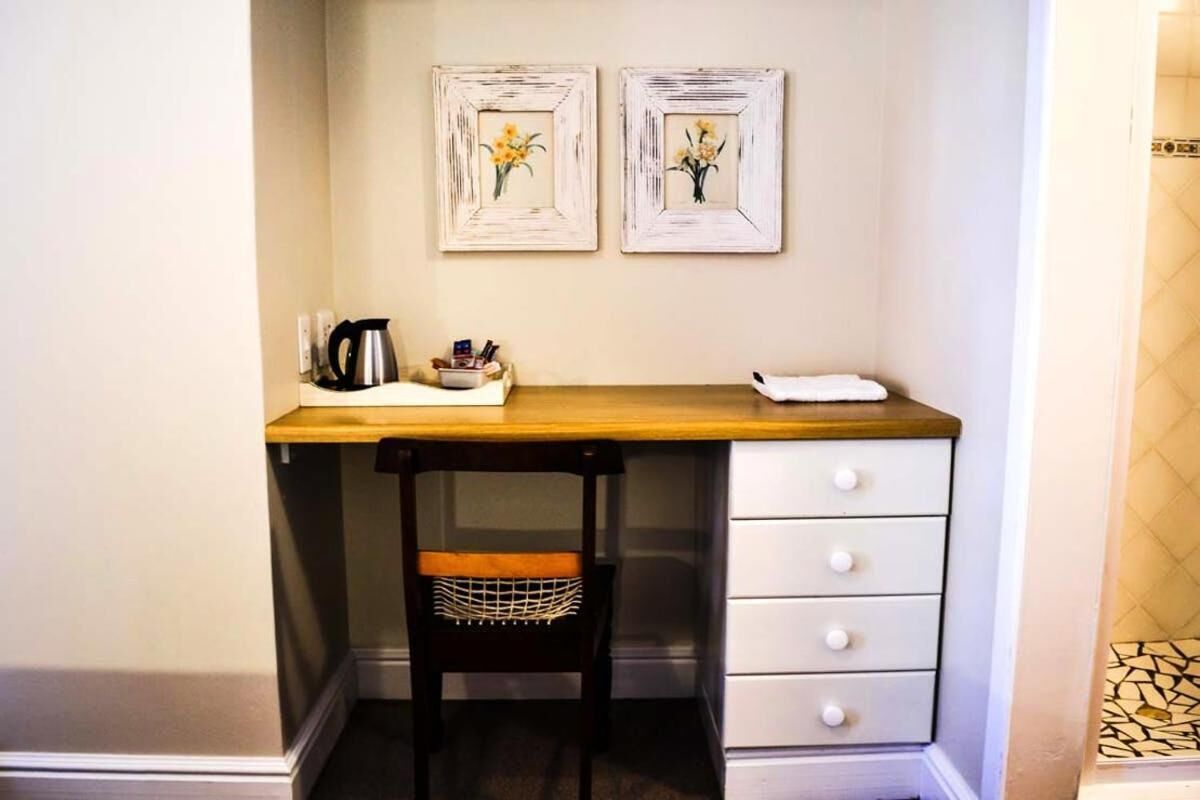 A compact workspace with a wooden desk, a chair with a mesh backrest, and a white drawer unit. Two framed floral paintings adorn the wall above the desk.