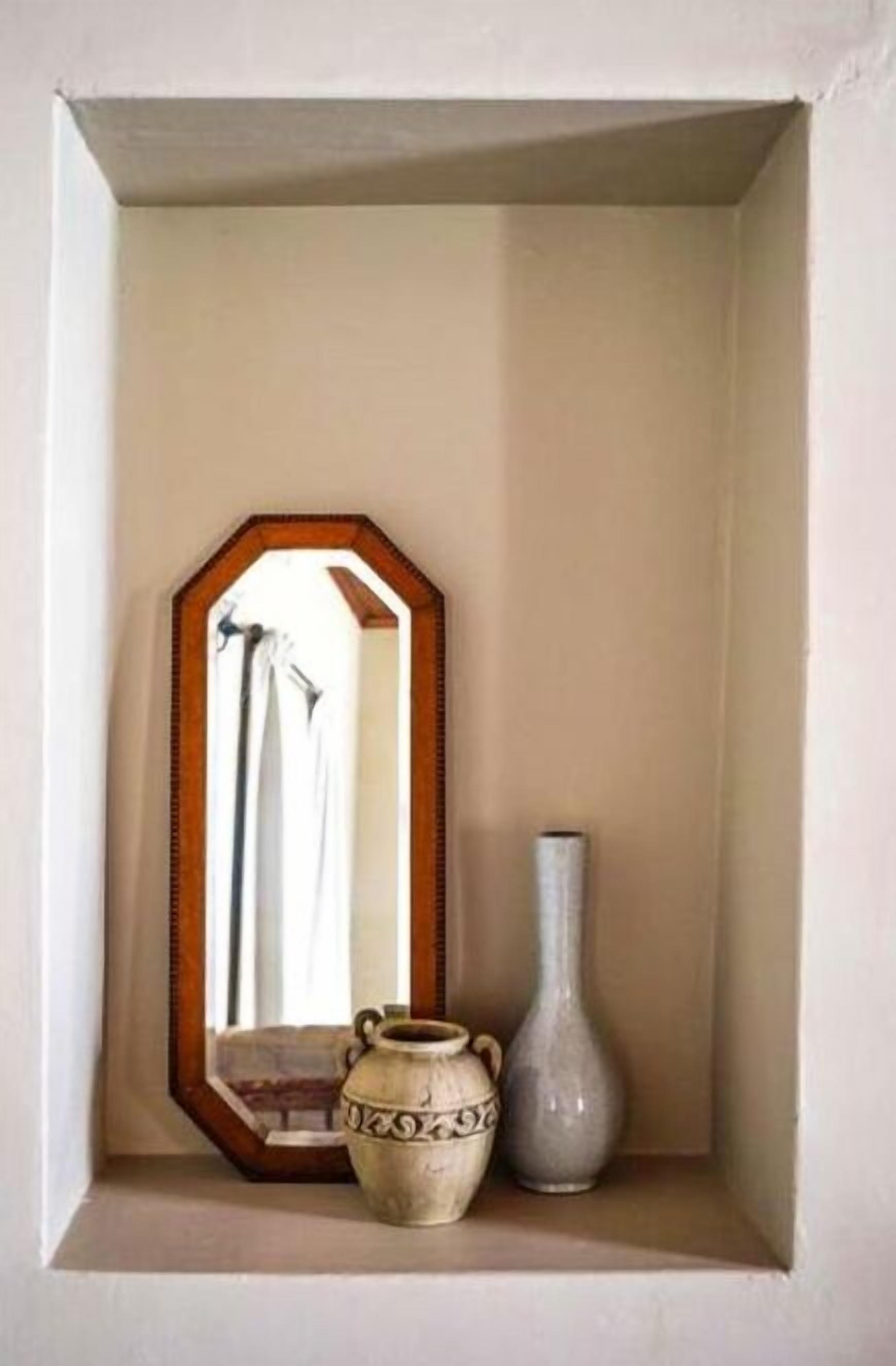 A small, white-framed shelf with a mirror, a white vase, and a grey vase.