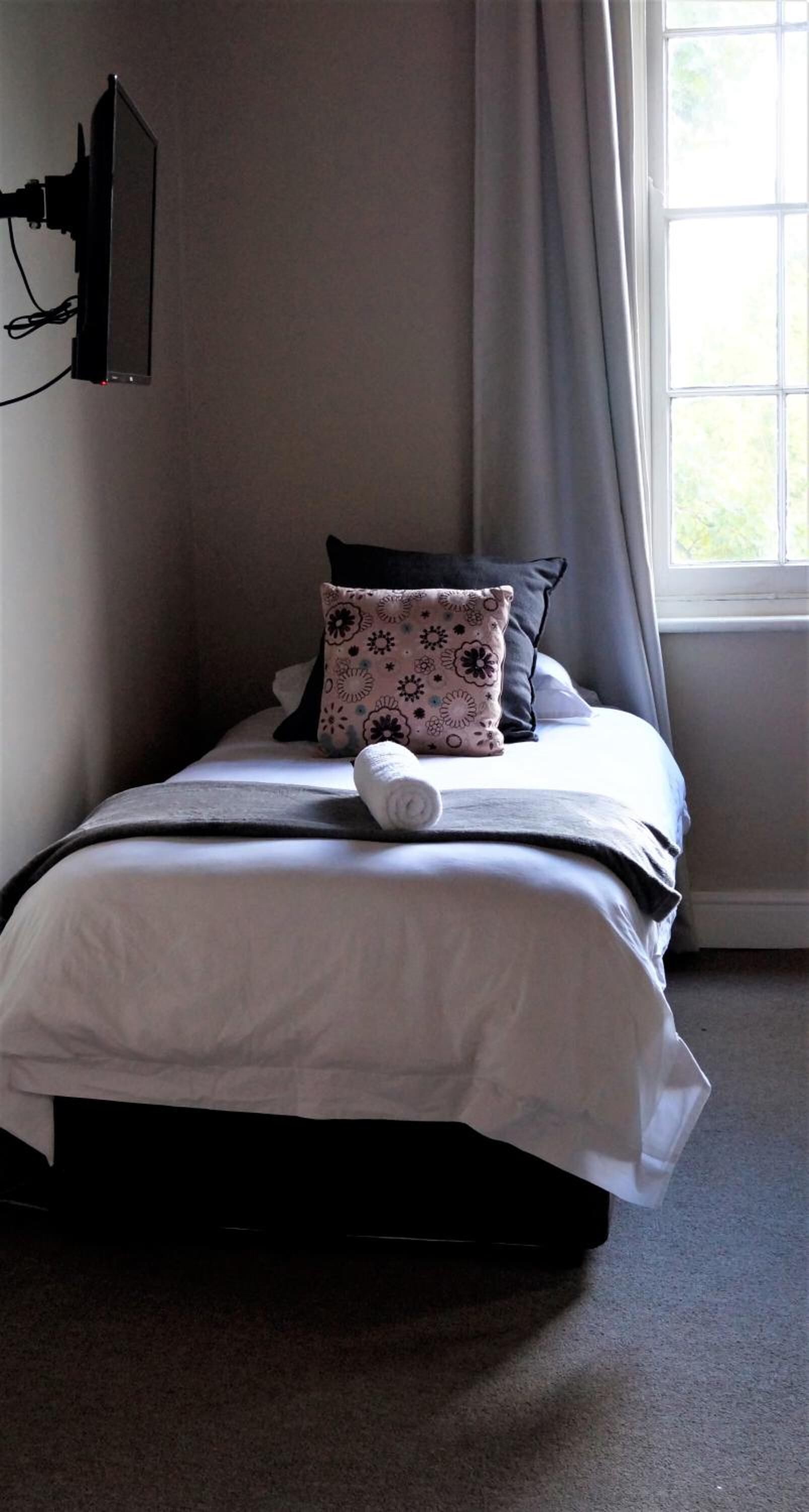 Una cama bien hecha con una colcha blanca, una almohada estampada y una almohada negra.