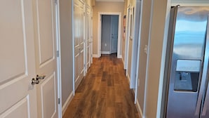 Un couloir doté d’un plancher en bois, de portes blanches et d’un réfrigérateur en acier inoxydable.