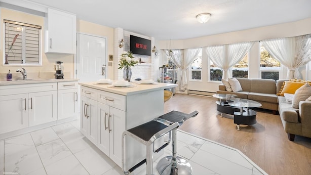 Una cocina moderna con armarios blancos, un comedor con mesa de vidrio y una sala de estar con sofá y televisor mostrando 'NETFLIX'.