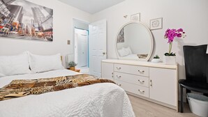 Un dormitorio con una cama, un tocador con espejo, una silla y una orquídea en maceta.