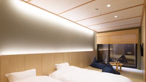 A modern hotel room with two beds, a wooden headboard, a small table, and a view of a traditional house through a large window. - Mibu-Juku (Kyoto)