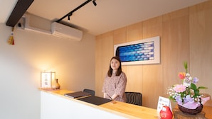 A reception desk with a laptop, a vase, a framed picture, a flower arrangement, and a sign indicating payment options. - Mibu-Juku (Kyoto)