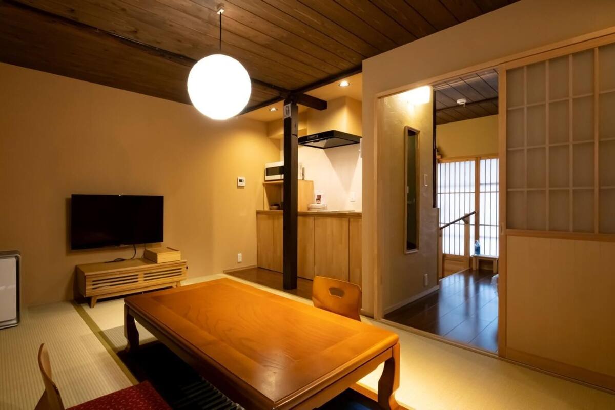 Une pièce de style japonais traditionnel, avec un sol recouvert de tatamis, une petite table en bois, un téléviseur et des portes coulissantes donnant sur un autre espace.