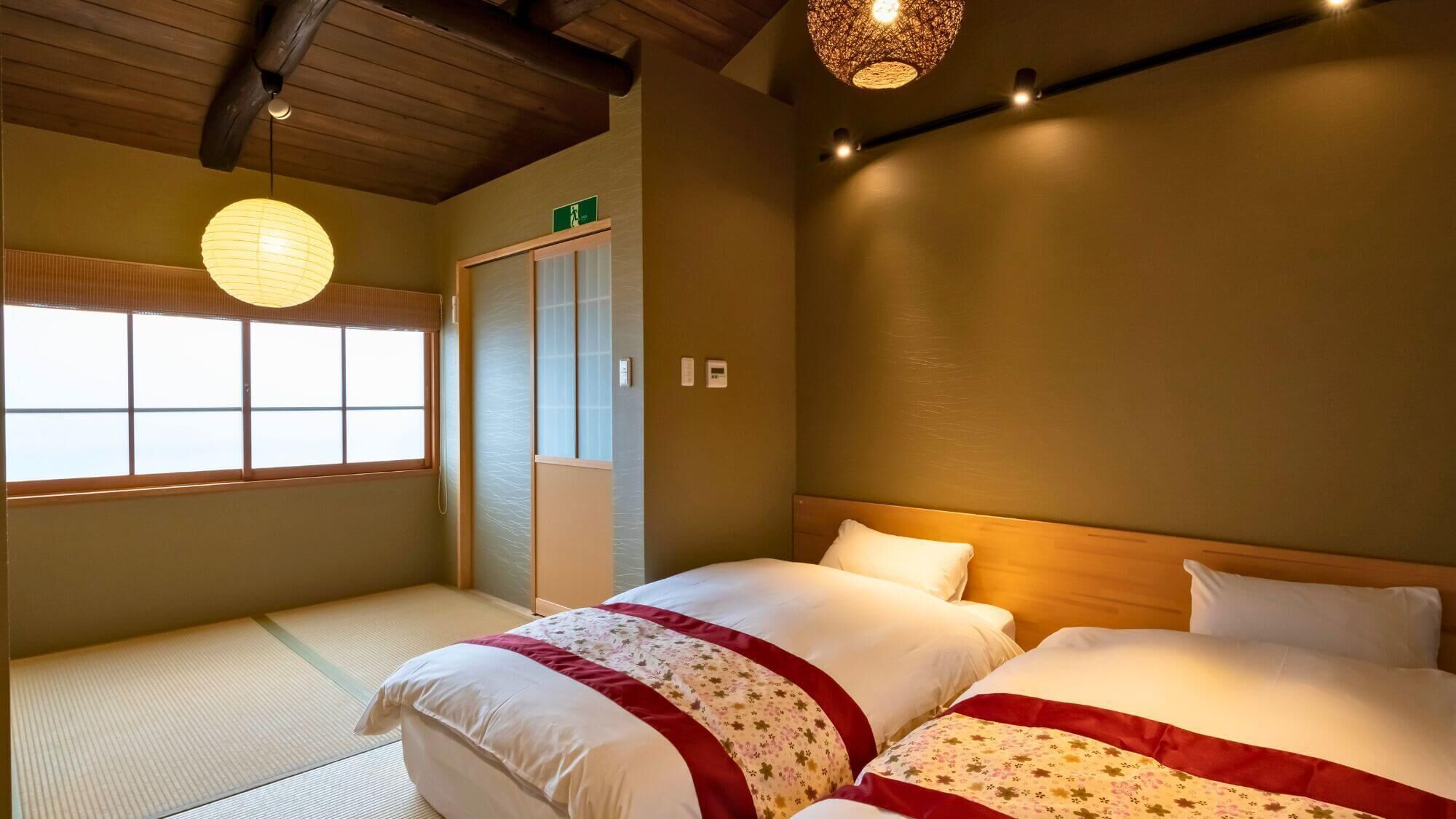 Et traditionelt japansk værelse med tatamimåtter, to senge med blomstret sengetøj, en shoji-skærmdør og en hængende papirlampe.