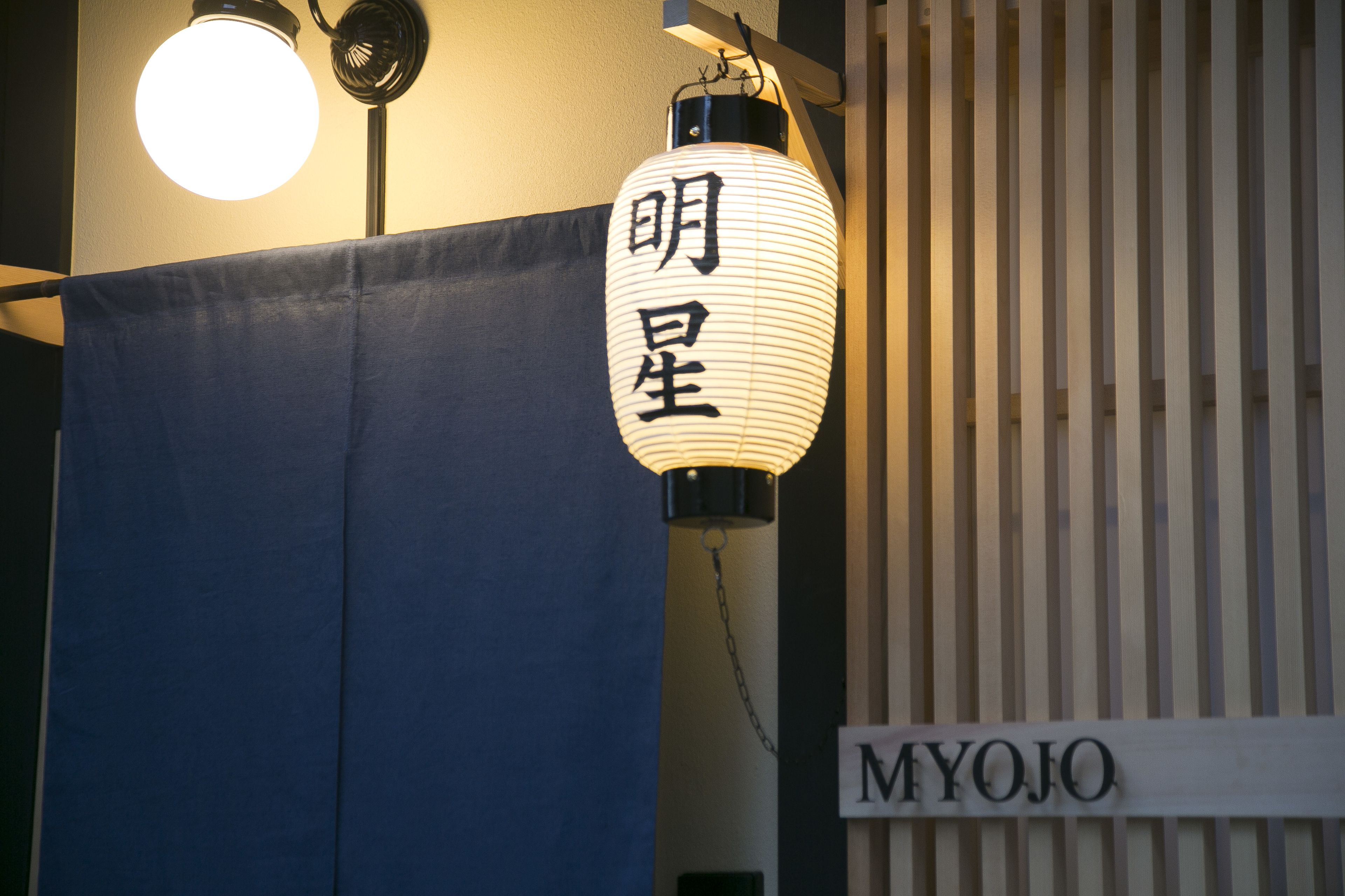 A hanging lantern with Japanese characters, a blue curtain, and a sign reading "MYOJO".