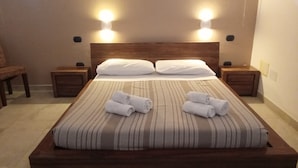 A neatly made bed with striped bedding and two pillows, two bedside tables with lamps, and a chair in the corner.