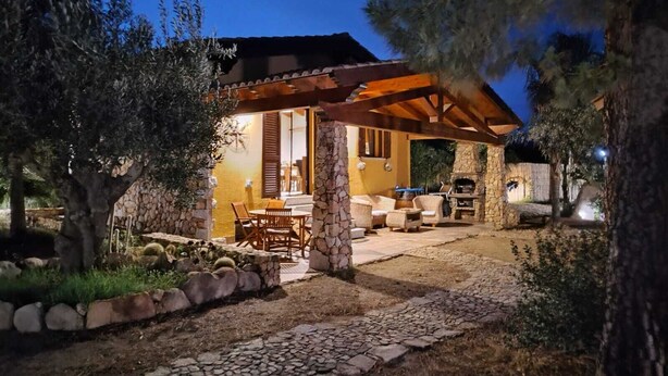 A stone-walled outdoor patio with a wooden pergola, stone seating, and a stone fireplace.