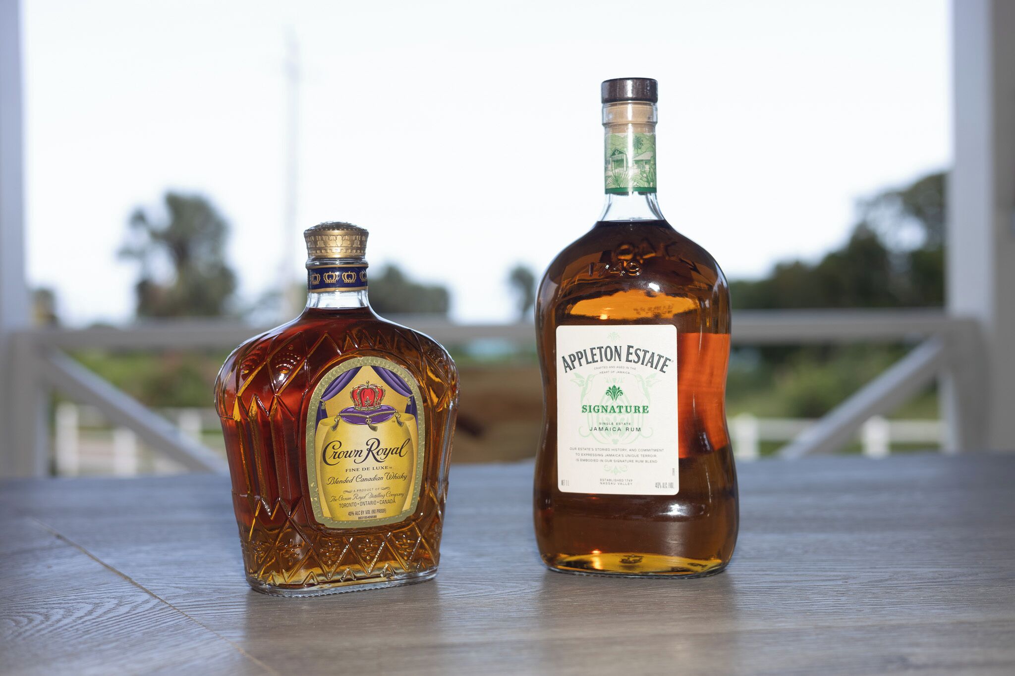 Dos botellas de ron sobre una mesa de madera con una barandilla al fondo.