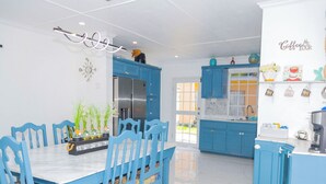 A modern kitchen with blue cabinets, a stainless steel refrigerator, and a dining area with blue chairs and a white table. - Treasure Beach Inn and Bar Room #1: Driftwood Queen (St. Elizabeth Parish)