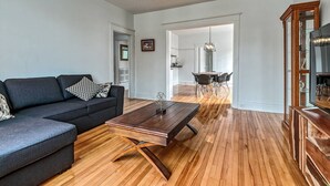 A modern living room with a dark grey sofa, a wooden coffee table, and a dining area with a glass table and chairs.
