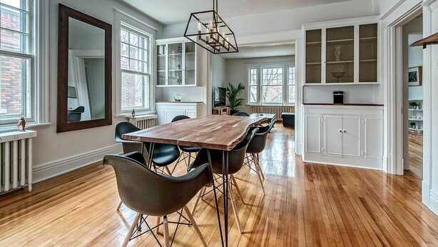 A spacious dining area with a wooden table and black chairs, large windows, and white cabinetry.