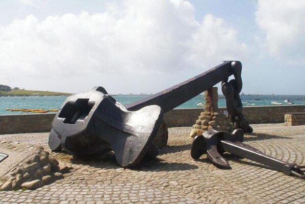 Een groot ankersculptuur langs een geplaveid pad aan de zee.