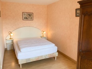 A bedroom with a bed, two bedside lamps, a nightstand, a wooden wardrobe, and a framed picture on the wall.