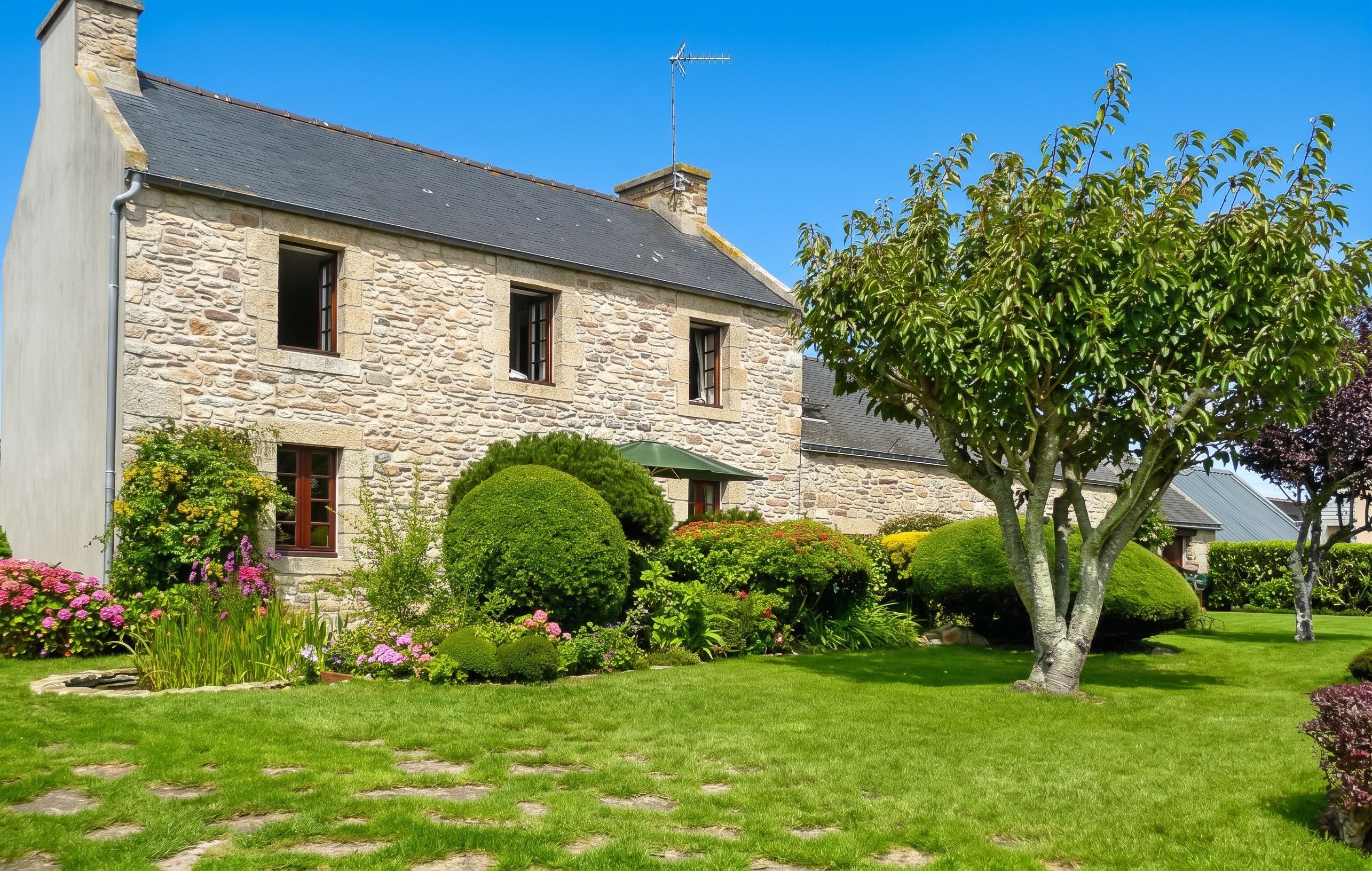 A stone building with a sloped roof, a chimney, and a flagpole.