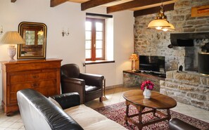 Un salon avec une cheminée, des meubles en cuir, un téléviseur et un mur en pierre.