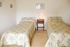 Een kleine, eenvoudige kamer met twee eenpersoonsbedden, een nachtkastje met een lamp en een ingelijst foto aan de muur.