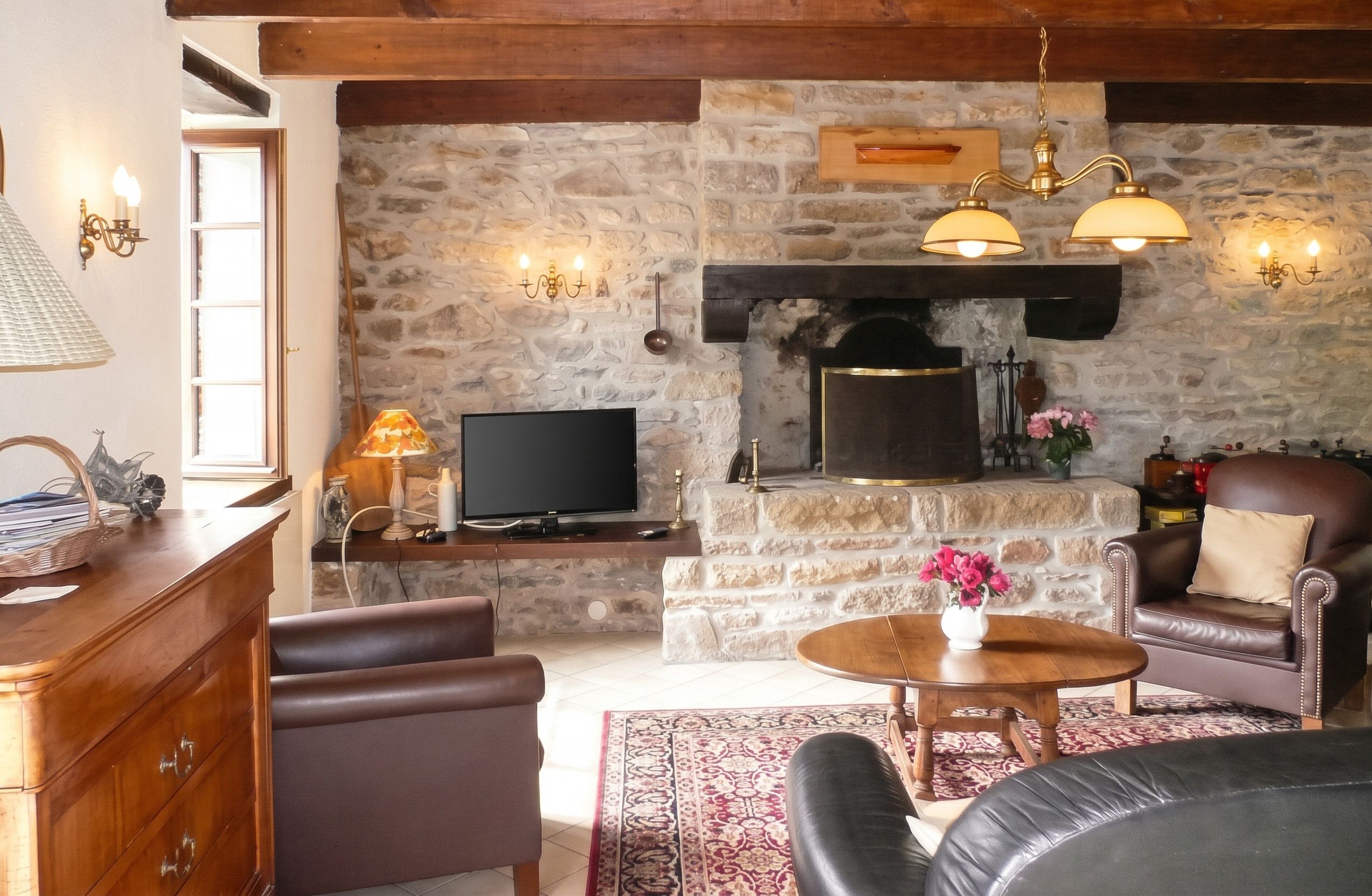 Ein gemütliches Wohnzimmer mit Kamin aus Stein, Ledermöbeln und einem Flachbildfernseher.