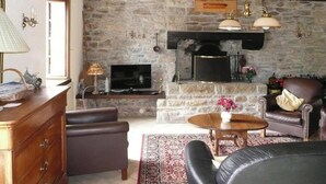 Ein Kamin aus Stein, ein Fernseher, Ledersofas, ein Holztisch und ein gemustertes Teppich.