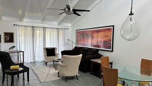 A modern living room with a ceiling fan, a dining area with a glass table, and a large abstract painting on the wall. - Downtown-Melbourne Beach-Dining-Cafes Walk to Everything (Melbourne)