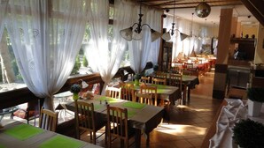 Un restaurant avec des tables et des chaises en bois, des rideaux blancs et des lustres suspendus.