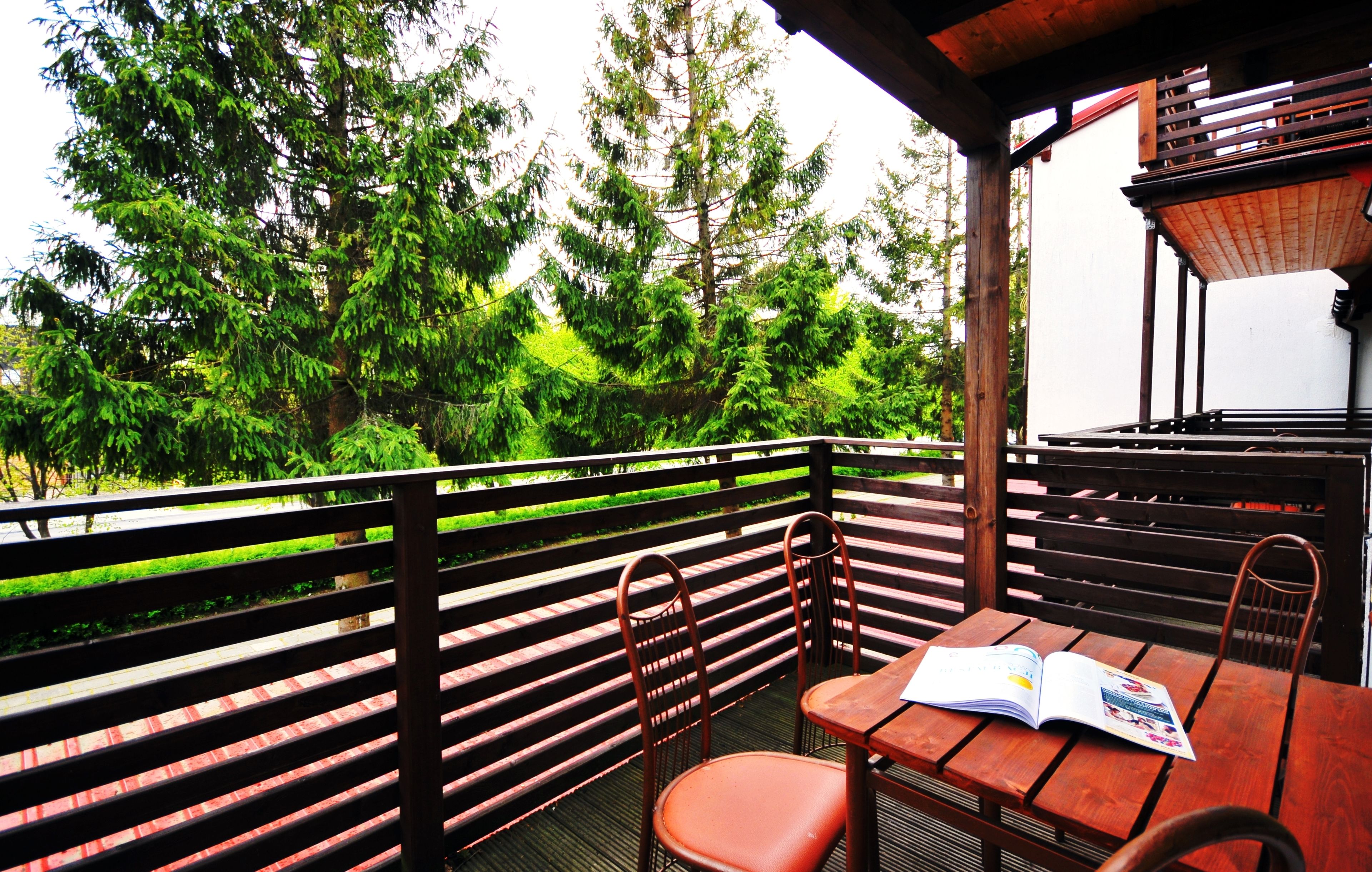 A wooden deck with a table and chairs, surrounded by lush greenery and trees.