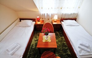Una habitación pequeña y ordenada con dos camas individuales, una mesa de madera con un florero y dos lámparas de noche.