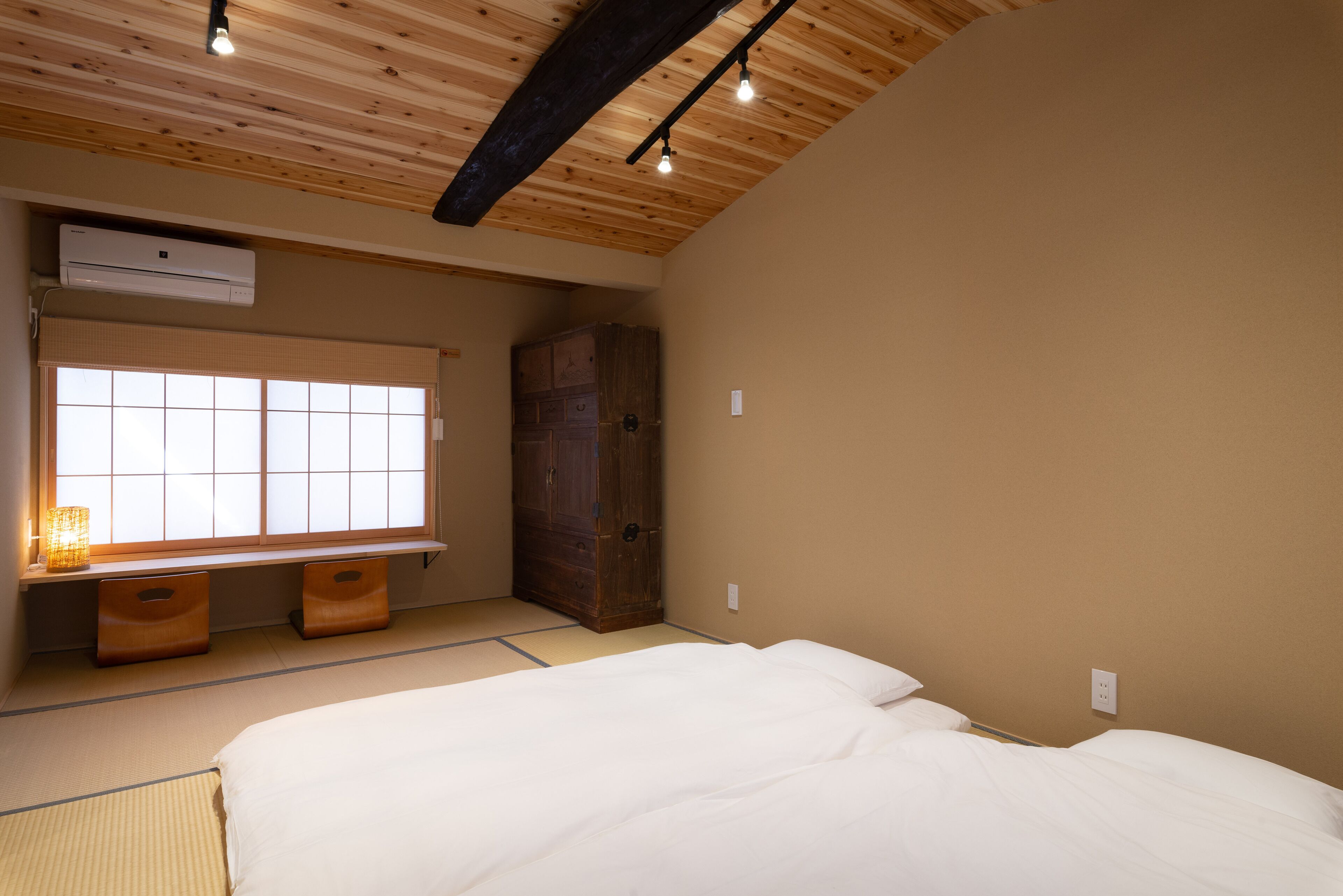 Un dormitorio con cama, ventana con persianas, armario de madera y una mesita de noche con lámpara.