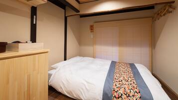 A small, neatly arranged room with a single bed, a wooden desk, and a traditional sliding door.