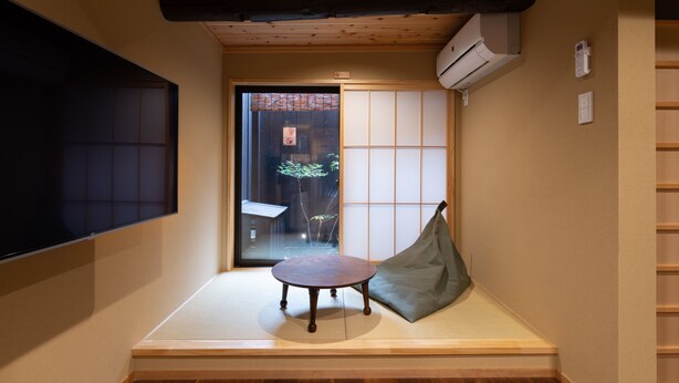 Um quarto japonês tradicional com tatames, uma mesa de madeira baixa e um assento almofadado verde.