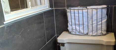 Un baño con azulejos oscuros, un inodoro blanco y una ventana con reja de metal.
