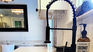 Una cocina con encimera de mármol, un lavamanos, un grifo y una botella de jabón para manos.