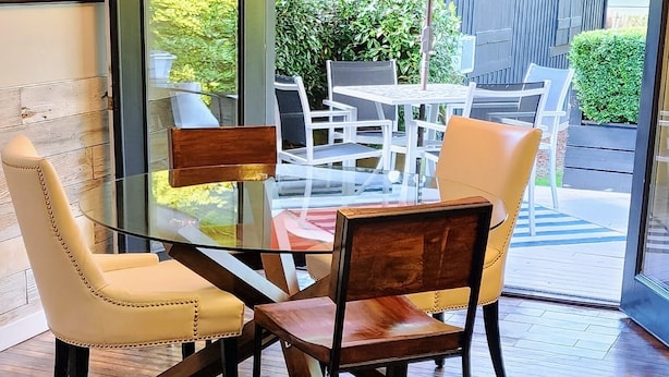 Un comedor moderno con una mesa y sillas de vidrio, piso de madera y vistas al exterior a través de grandes puertas de cristal.